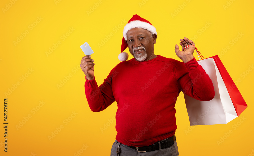 Christmas sales and shopping. Senior black man with shopper bags holding credit card, wearing Santa hat