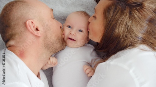 Happy family. Newborn baby with happy parents, top view. Healthy newborn baby in a white t-shirt with mom and dad. Close up Faces of the mother, father and infant baby. Cute Infant boy and parents