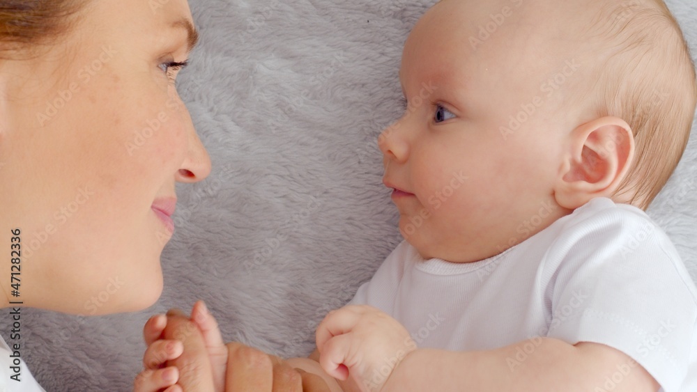 Happy newborn baby with his mother. Healthy newborn baby in a white t-shirt with mom. Closeup Faces of the mother and infant baby. Cute Infant boy and parent, top view. Happy family portrait Happy newborn baby with his mother. Healthy newborn baby in a white t-shirt with mom. Closeup Faces of the mother and infant baby. Cute Infant boy and parent, top view. Happy family portrait