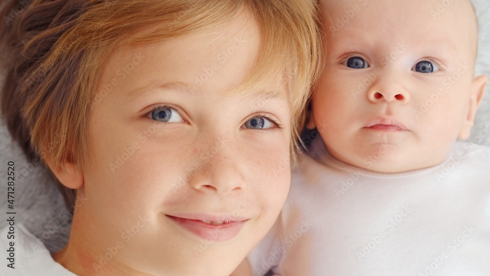 Smiling faces of the brothers, top view. Happy newborn baby with his brother. Healthy newborn baby in a white t-shirt with brother. Closeup Faces of the brothers. Happy family Smiling faces of the brothers, top view. Happy newborn baby with his brother. Healthy newborn baby in a white t-shirt with brother. Closeup Faces of the brothers. Happy family