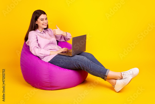 Full length profile side photo of youth girl show thumb-up advertise promo use laptop isolated over yellow color background