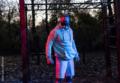 Tough strong muscular man wearing a workout mask standing below horizontal ladder in the park taking a break during workout