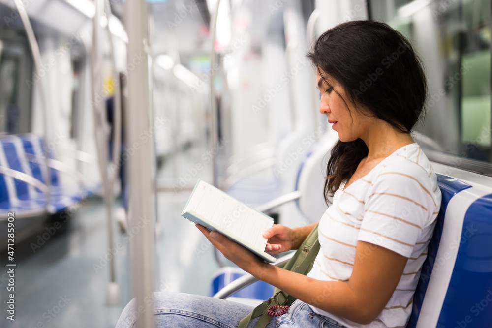  woman reading book while sitting on bench in metropolitan train.