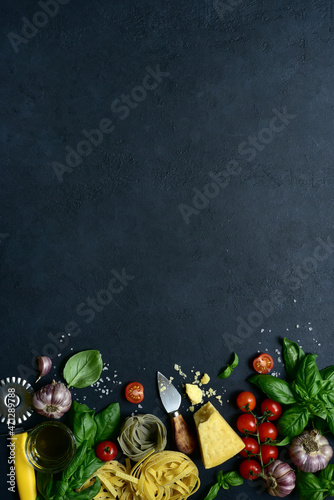 Culinary background with traditional ingredients of italian cuisine : pasta, tomatoes, garlic, olive oil, parmesan cheese, basil. Top view with copy space.