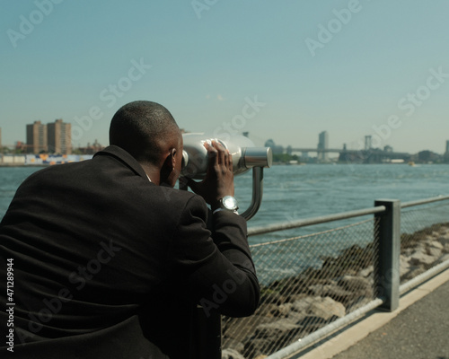 USA, New York City, Man in suit looking at city through coin operated binoculars
