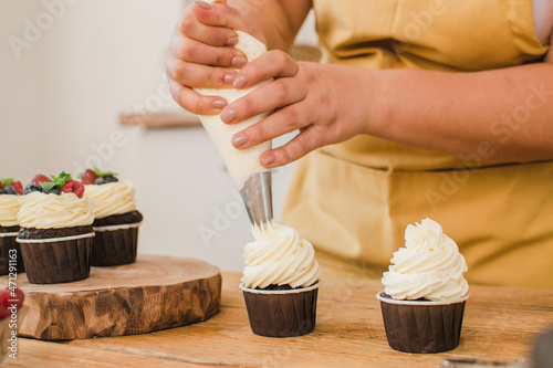 Canvas-taulu Women's hands decorate cupcakes with cream