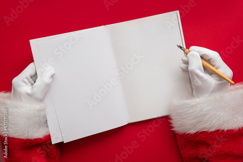 Santa Claus writing a naughty or nice list in a book. blank page mock up photo