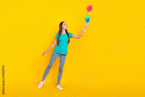 Photo of dreamy lady hold fluffy duster look empty space wear teal t-shirt jeans shoes isolated yellow color background