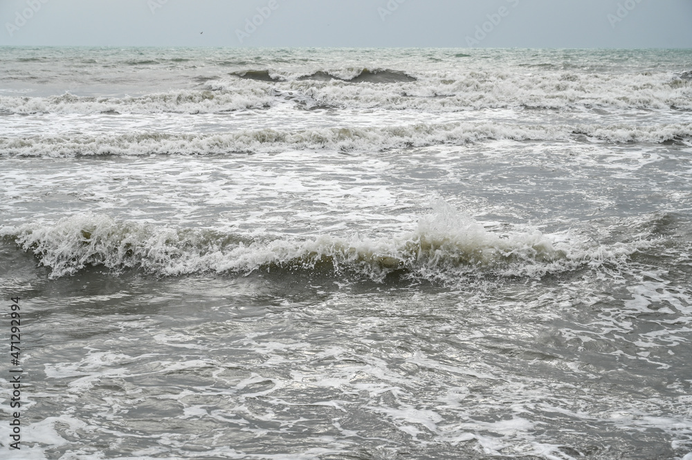 Muddy sea water after the rain. Stormy weather on the coast. Waves of the sea with sandy brown and grey color. 
