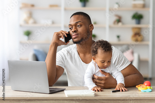 Busy Black Man Working Remotely At Home With Little Baby On Hands