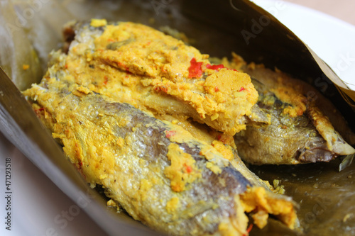 Pepes ikan, or steamed fish with herbs then wrapped in banana leaf. Indonesia traditional food. Wooden background. photo