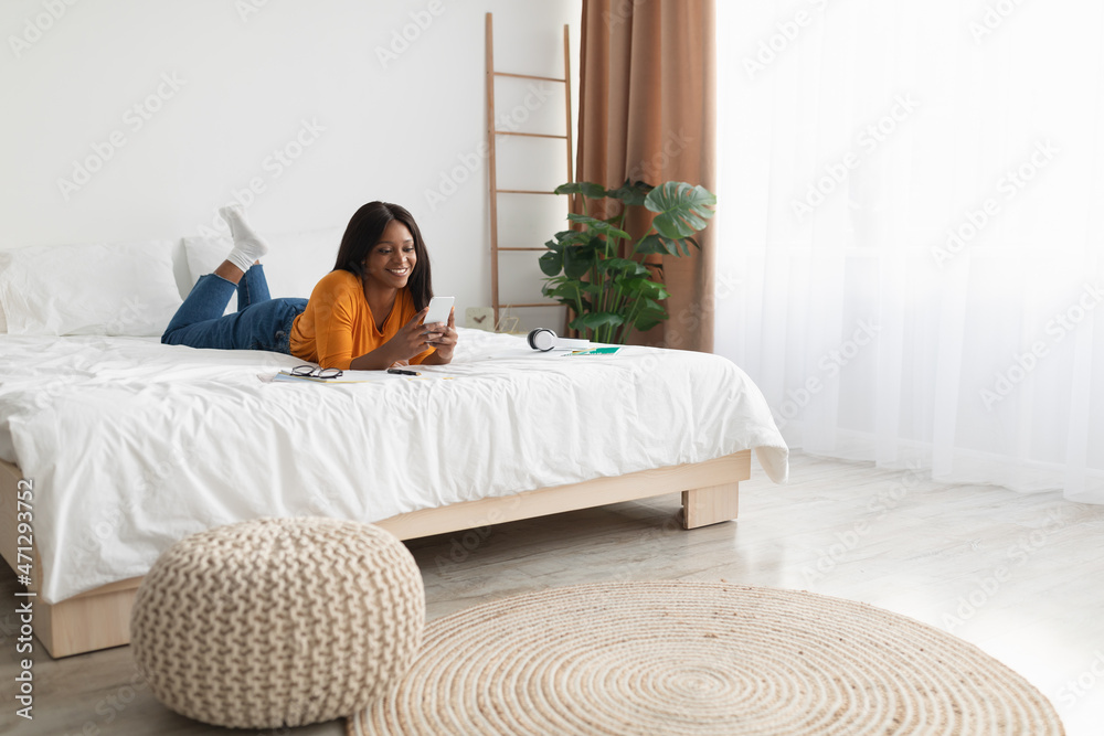 African American Female Using Phone Lying In Modern Bedroom African American Female Using Phone Lying In Modern Bedroom