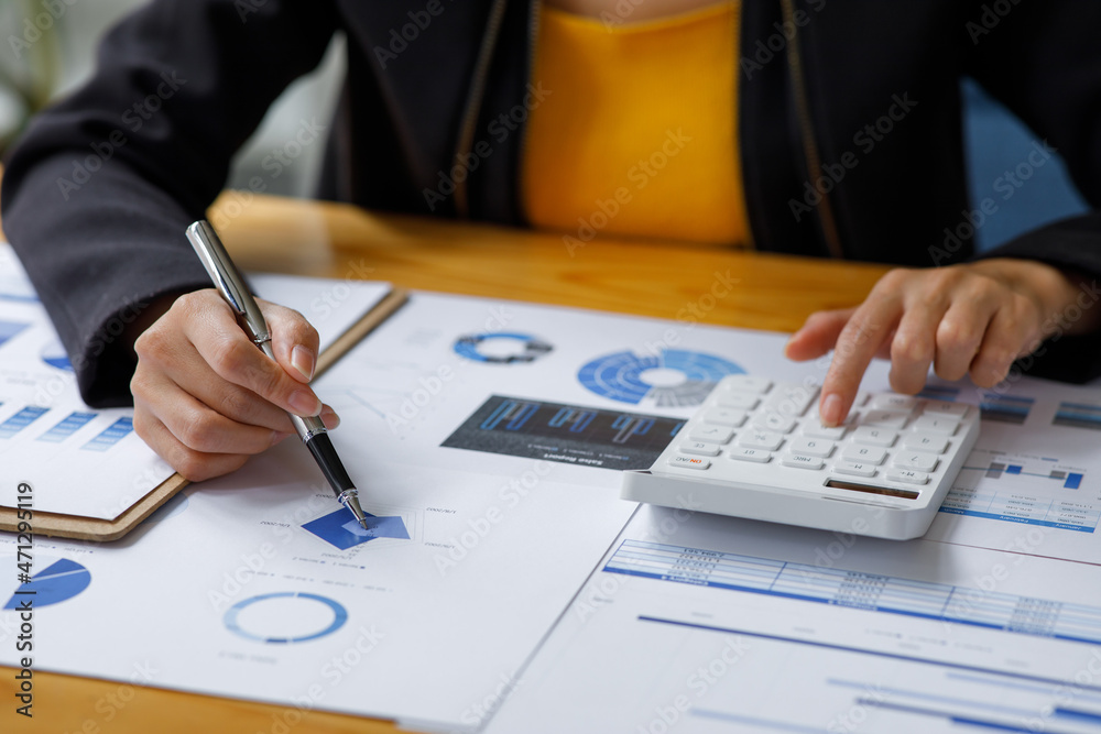 Close up a Business woman using calculator and laptop for doing math finance on a wooden desk, tax, accounting, statistics, and analytical research concept Close up a Business woman using calculator and laptop for doing math finance on a wooden desk, tax, accounting, statistics, and analytical research concept