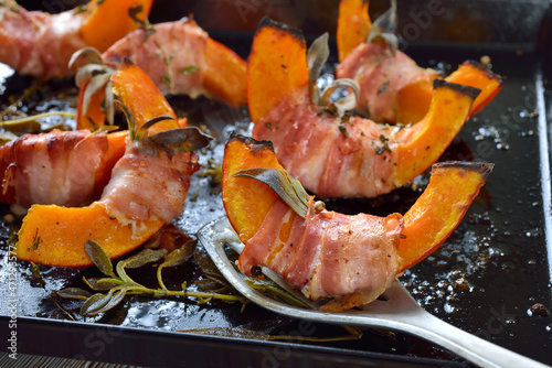 Hokkaido-Kürbisschnitten im Salbei-Speckmantel aus dem Ofen – Pumpkin gaps wrapped in bacon with sage leaves and thyme, baked in olive oil with pepper and salt photo