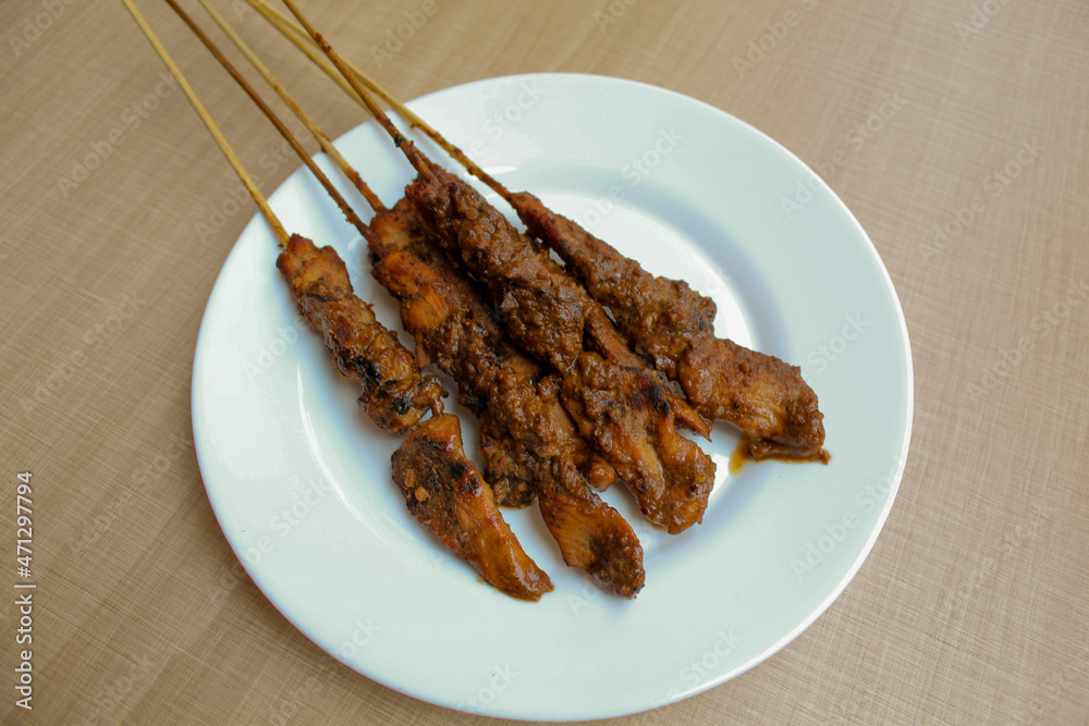 Chicken satay covered by peanut sauce, with bamboo skewers. Indonesian traditional food. On a white plate. Isolated on white background Chicken satay covered by peanut sauce, with bamboo skewers. Indonesian traditional food. On a white plate. Isolated on white background