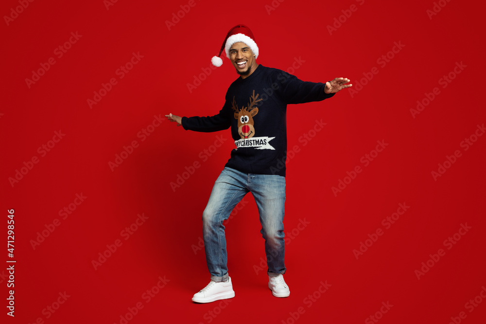 Carefree black guy in Santa hat dancing alone on red