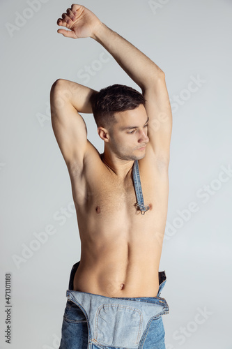Portrait of young handsome sportive shirtless man in jeans posing isolated on gray studio background.