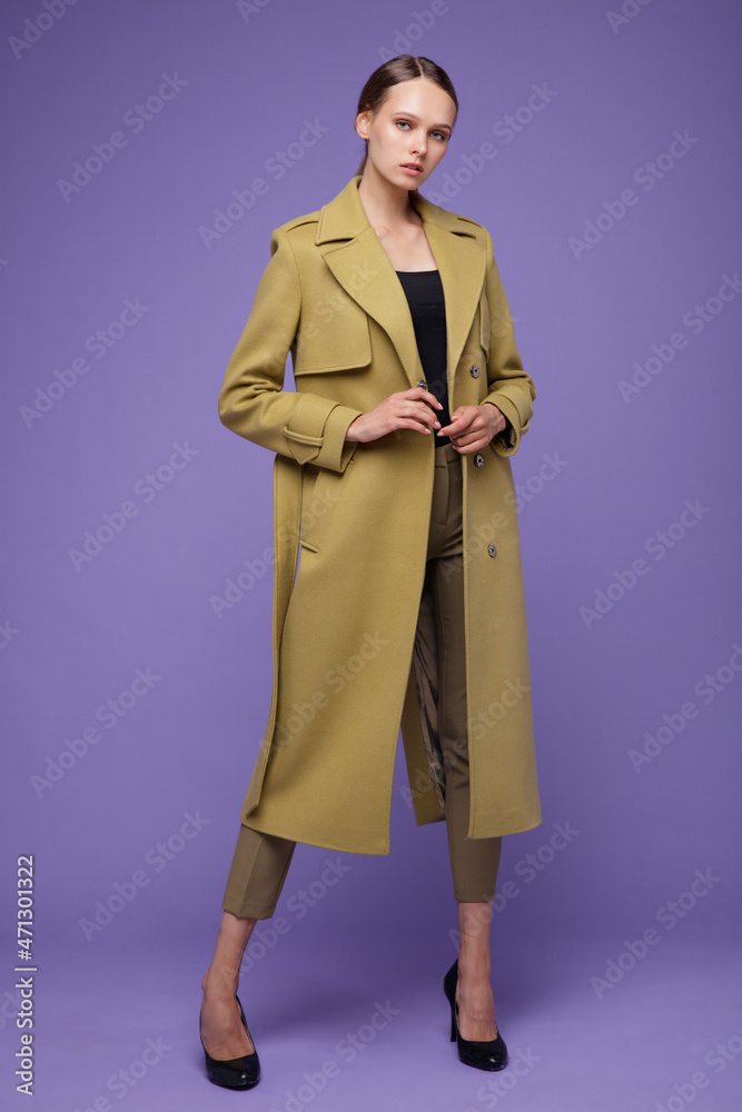 High fashion photo of a beautiful elegant young woman in a pretty yellow mustard coat, pants, trousers posing on a purple lavender background. Studio shot, portrait. High fashion photo of a beautiful elegant young woman in a pretty yellow mustard coat, pants, trousers posing on a purple lavender background. Studio shot, portrait.