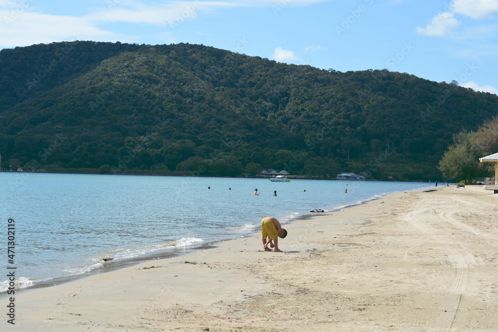 A tiny boy wearing yellow pants playing sand on the beach at Laem Sing Beach. A tiny boy wearing yellow pants playing sand on the beach at Laem Sing Beach.