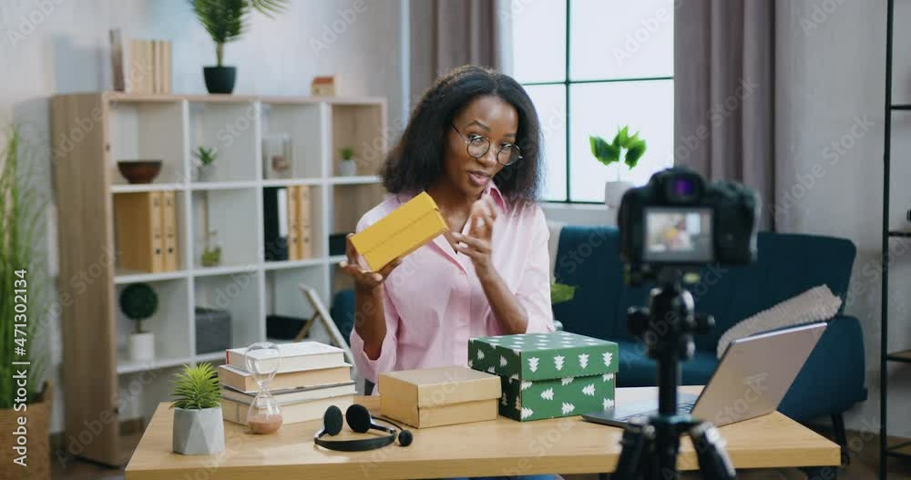 Blogging concept where charming smiling happy young african american woman showing gift boxes on camera during recording vlog for her internet channel Blogging concept where charming smiling happy young african american woman showing gift boxes on camera during recording vlog for her internet channel