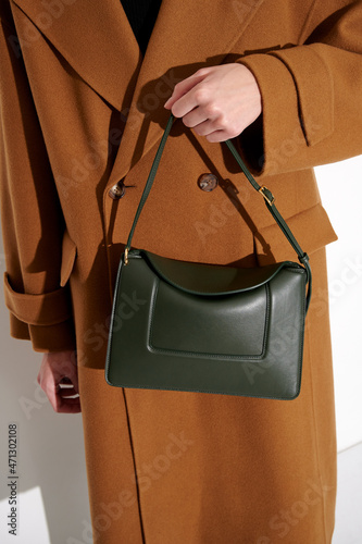 Woman in a brown  coat with luxury green leather handbag. Fashionable shoulder bag. White background. Vertical photo.
