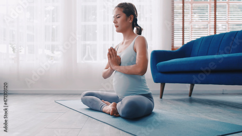 Asian pregnant woman doing yoga exercises at home.