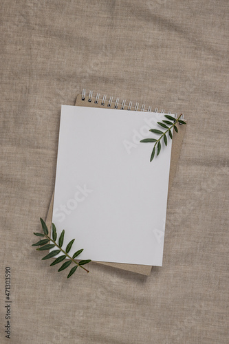 Summer wedding stationery mock-up scene. Blank greeting card, craft paper envelope and green branches on linen textile background.
