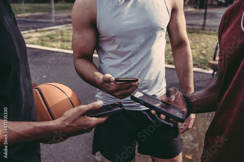 USA  Pennsylvania  Philadelphia  Male friends looking at smart phones at basketball court