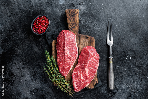 Fresh Raw Top Blade or flat iron beef meat steaks on a butcher cutting board. Black background. Top View