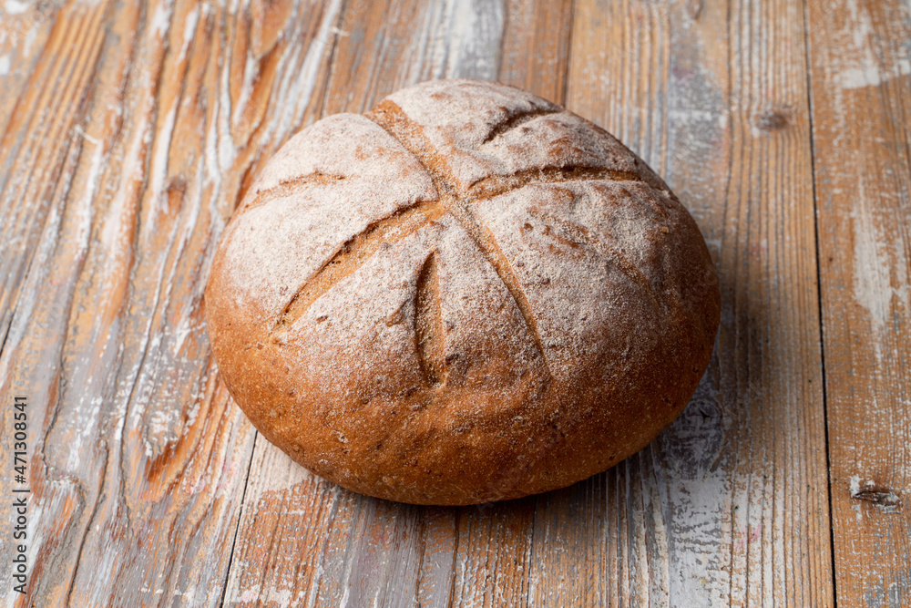 Appetizing round loaf of bread decorated with cuts on wooden table, rustic style photo with text space, spikes laying around