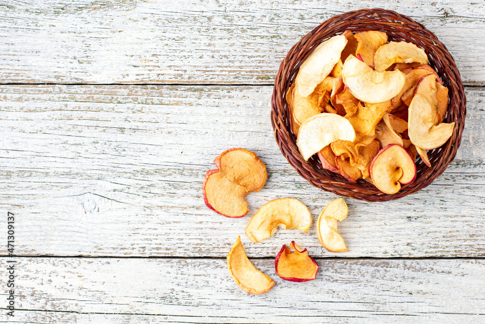Fototapeta premium A pile of dried slices of apples in wicker basket on white wooden background. Dried fruit chips. Healthy food