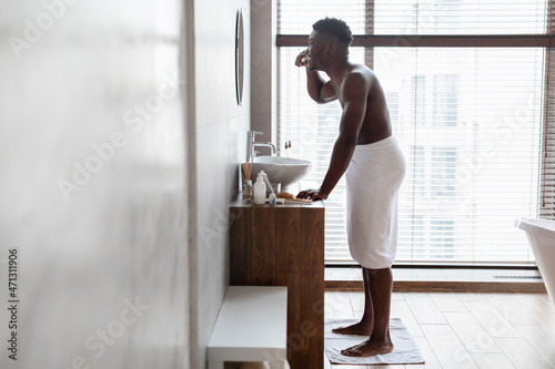 Cheerful Black Guy Cleaning Teeth With Toothbrush Standing In Bathroom