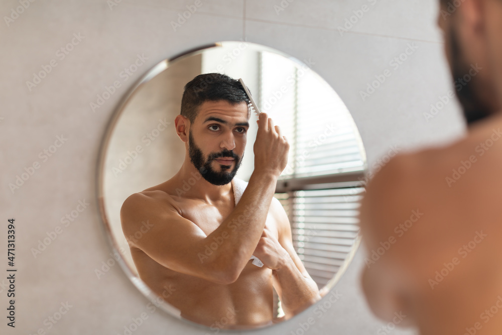 Back rear view of guy looking in mirror brushing hair - obrazy, fototapety, plakaty 