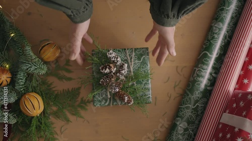 top view of the decorator's desktop Fully visible the table with the decorations. Female hands put and finalize Christmas gift wrapped in craftool paper on a wooden table photo