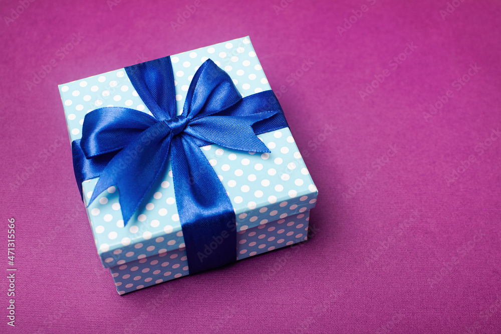Blue gift box with a bow on a violet background. Holiday greeting card. Blue gift box with a bow on a violet background. Holiday greeting card.
