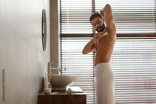 Handsome young guy using applying deodorant in bathroom