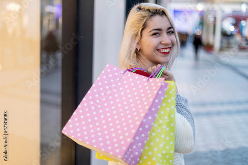 beautiful young blonde woman smiling with shopping bags outside
