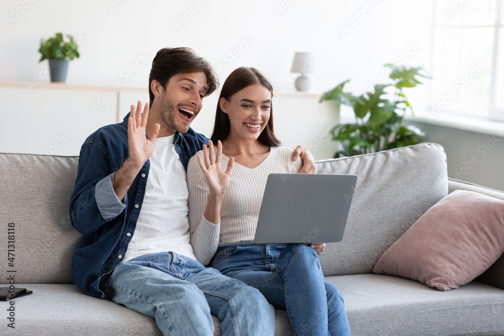 Happy european young husband and wife waving hands to webcam laptop, rejoice at online meeting and video call Happy european young husband and wife waving hands to webcam laptop, rejoice at online meeting and video call