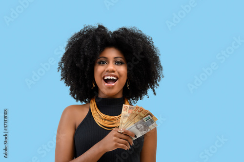 woman smiling holding brazilian money bills, positively surprised, space for text, person, advertising concept, isolated on blue background