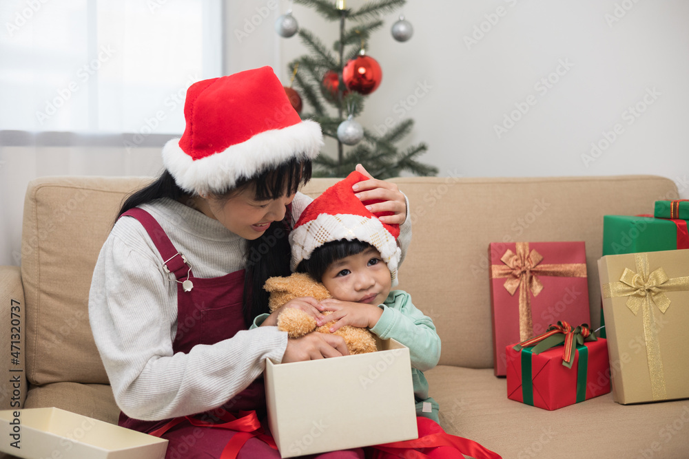 Asian family Mother giving the teddy bear to child. Happy moment Mom and son in christmas festival. They dressing christmas theme with decorative pile gift box on sofa. Giving present each other.