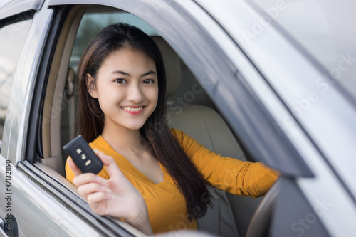 Young beautiful asian women getting new car. she very happy and excited looking outside window in hand holding car key. Smiling female driving vehicle on the road on a bright day © Chanakon