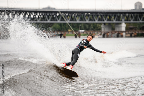 active young woman energetically riding wakeboard on the wave holding rope with her hand
