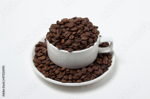 White cup overflowing with coffee beans on a white background. Freshly roasted coffee beans
