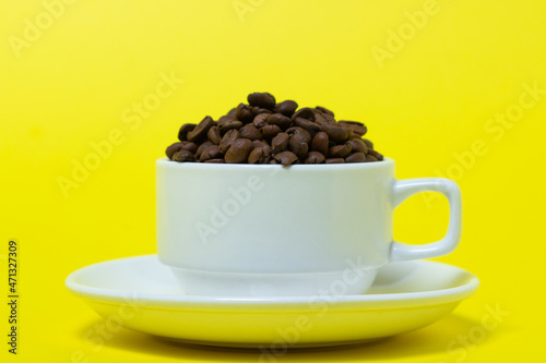 Cup filled with coffee beans on a yellow background. Freshly roasted coffee beans. Excessive consumption of caffeine