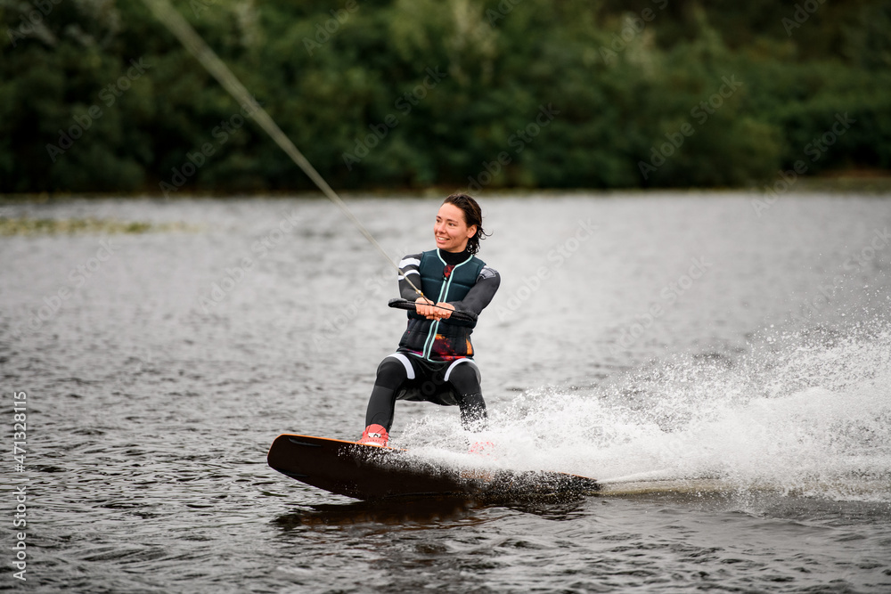 Obraz premium sportive woman wakeboarding on board on the river water on summer day