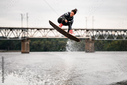 young woman holding rope and professionally jumping over splashing water on wakeboarding board