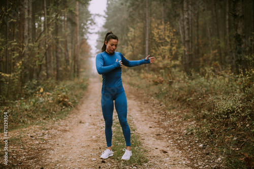 Young woman in blue track suit stretching before workout in the autumn forest