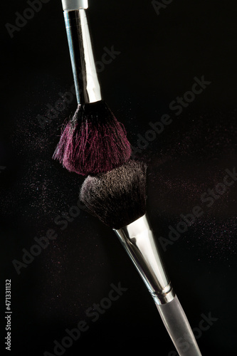 Cosmetic brushes in motion on a dark background a scattering of colored powder 