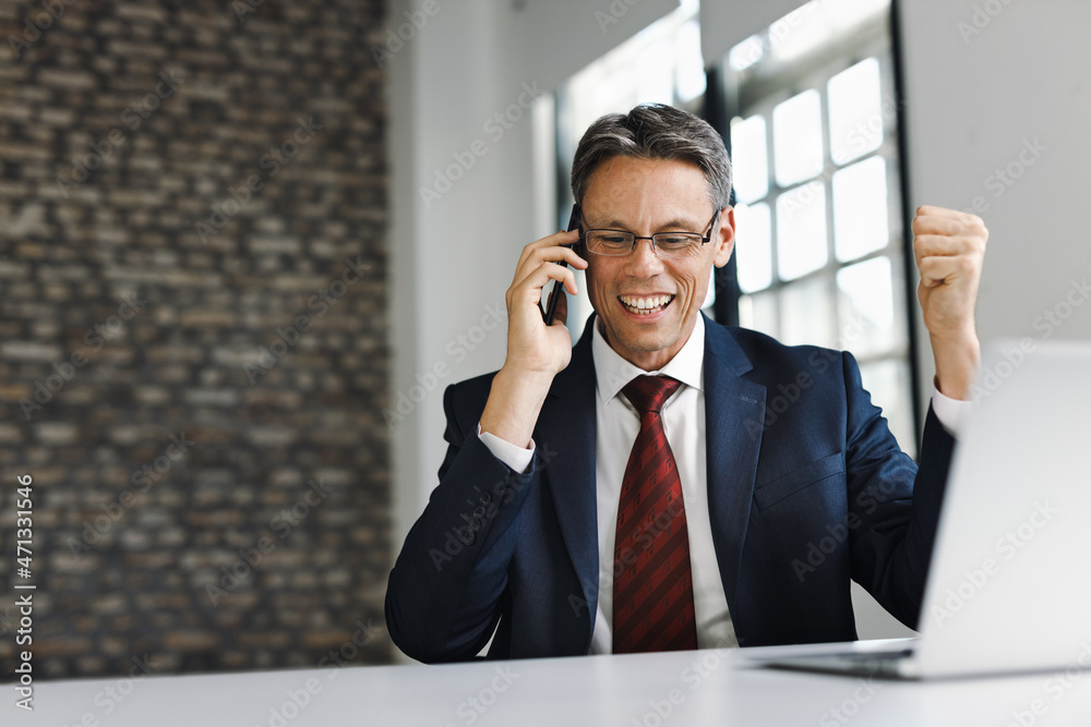 Happy businessman talking on smart phone while working on laptop in the office