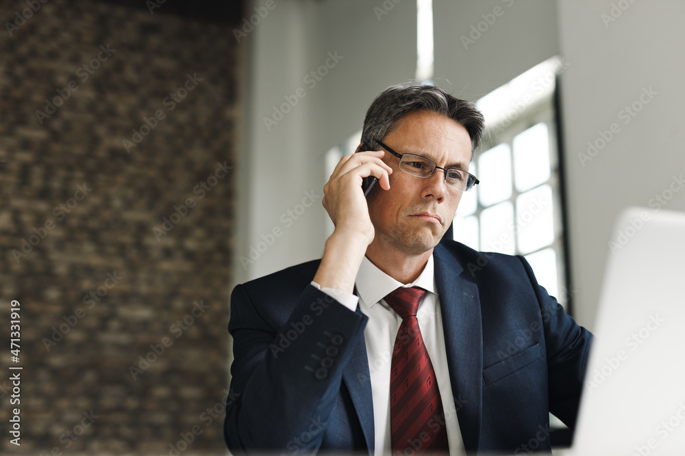 Businessman talking on smart phone while working on a computer in his office Businessman talking on smart phone while working on a computer in his office